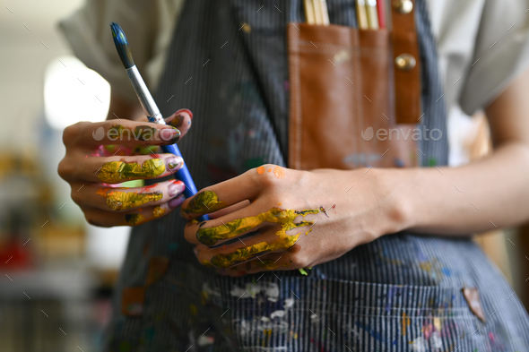 Artist hands soiled with watercolor paints holding brushes and smiling to camera.