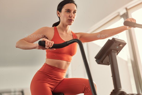 Fit female athlete exercising on elliptical fitness machine in gym