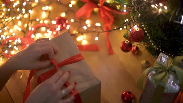 Women's hands take a large gift box under the Christmas tree