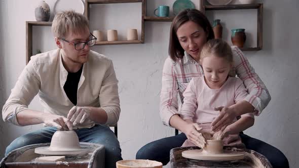 Mom and Dad Teaching Child Daughter To Shape Clay on a Spinning Wheel