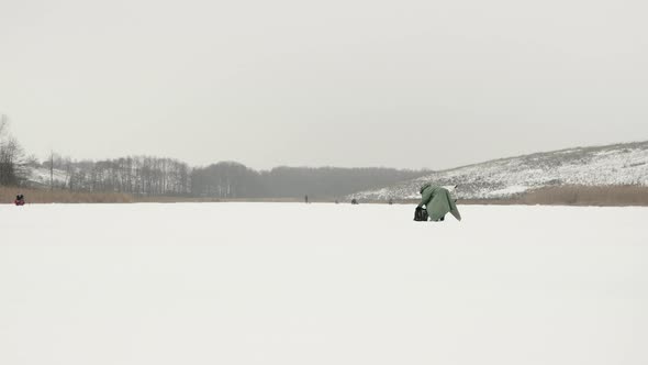Winter fishing concept. Fisherman with ice drill on frozen pond alt