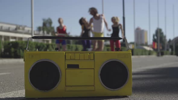 Retro Tape Recorder Standing on Asphalt with Four Caucasian Sportive People Doing Fitness Exercises alt