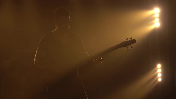 Silhouette of the Young Guy Playing the Electric Guitar on Stage in a Dark Studio with Smoke and alt