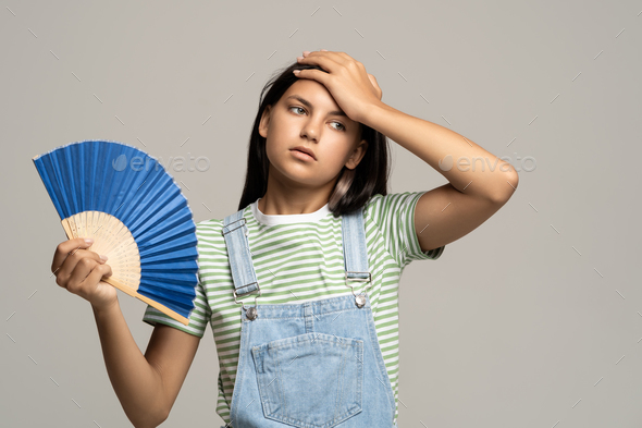 Sweaty teenage girl touching forehead using paper fan suffer from heat cooling in hot summer weather