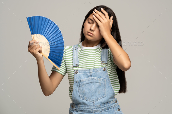Sweaty teenage girl touching forehead using paper fan suffer from heat cooling in hot summer weather
