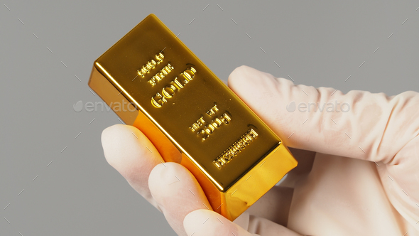 Gold bar in hand and wear latex glove isolated on grey background.