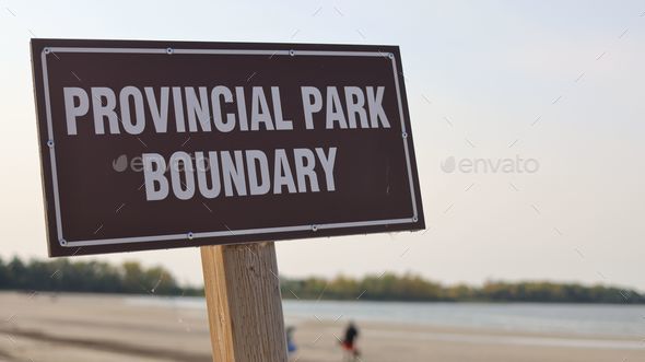 White font lettering Provincial Park Boundary on a brown sign with blur beach and lake background.