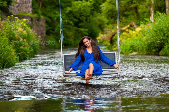 a joyful young woman swings on a rope swing across a fast-flowing