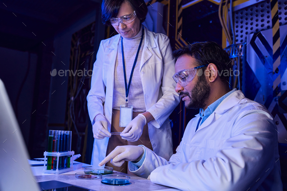 indian scientist pointing at petri dishes with samples of otherworldly life near colleague in lab