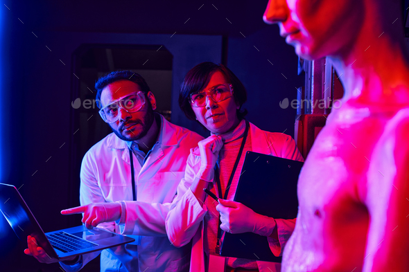 indian scientist pointing at laptop near thoughtful colleague and alien in discovery center
