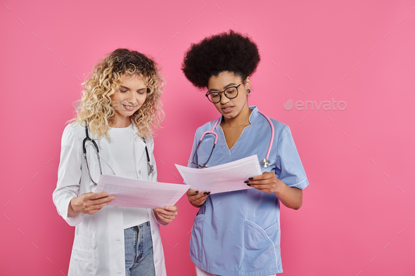 happy female oncologists, interracial doctors on pink backdrop, breast cancer awareness, diagnosis