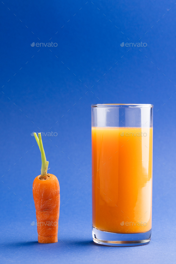 Close up of carrot and glass of carrot juice with copy space on blue