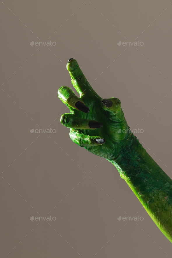 Vertical image of green monster hand with black nails making gesture on