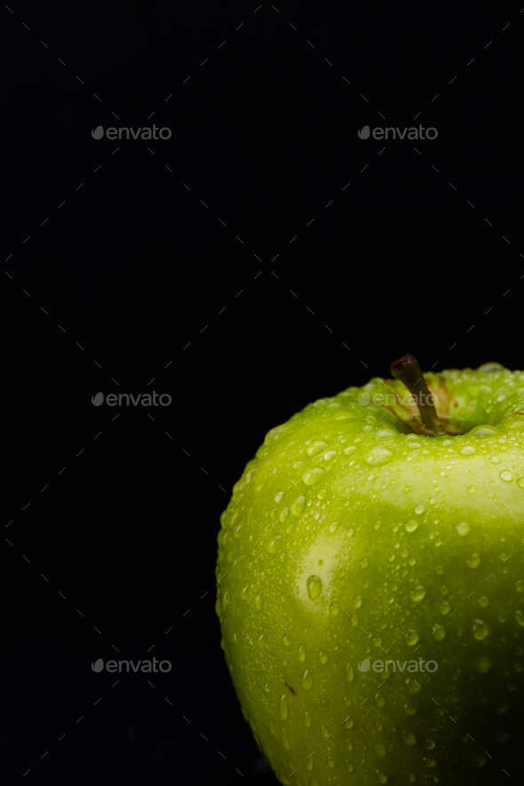 Micro close up of green apple with water drops and copy space on black background