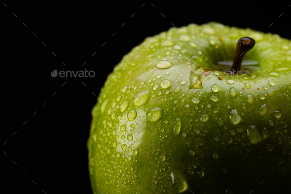 Micro close up of green apple with water drops and copy space on black background