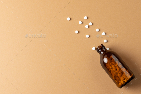 Composition of brown glass pill bottle spilling white pills on