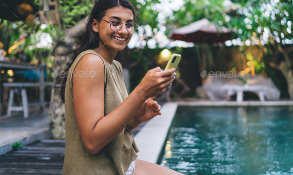 Content ethnic woman browsing smartphone on poolside