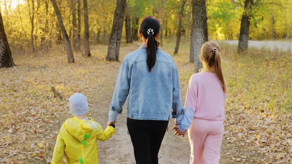 Mother and Two Children Walking in the Park and Enjoying the Beautiful Autumn Nature alt