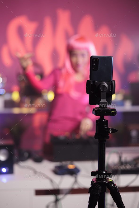 Artist with pink hair performing electronic song at turntables while filming music process