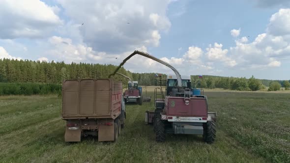 Drone view of two Combines harvesting and trucks on grass field. 40 alt