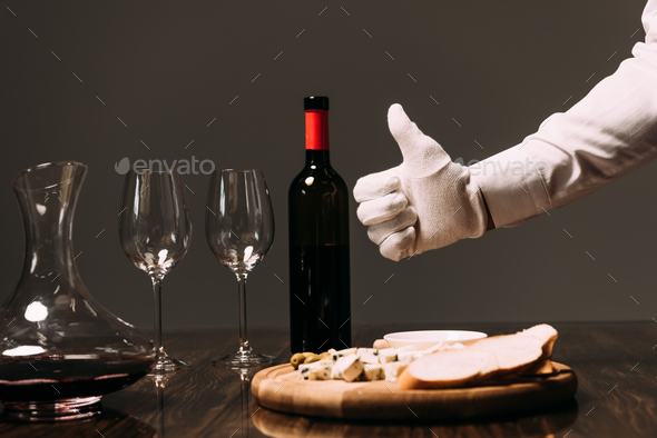 cropped view of waiter in white glove showing thumb up near table with food and wine