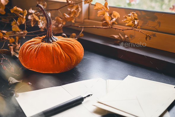 Cozy autumn still life with pumpkin, sheets of paper, fountain pen and burning candle on windowsill
