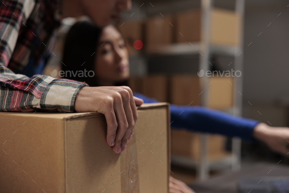 Postal wroker holding box while managing inventory with coworker
