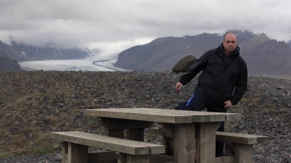Man sitting at Picnic table with a mountain in the background alt