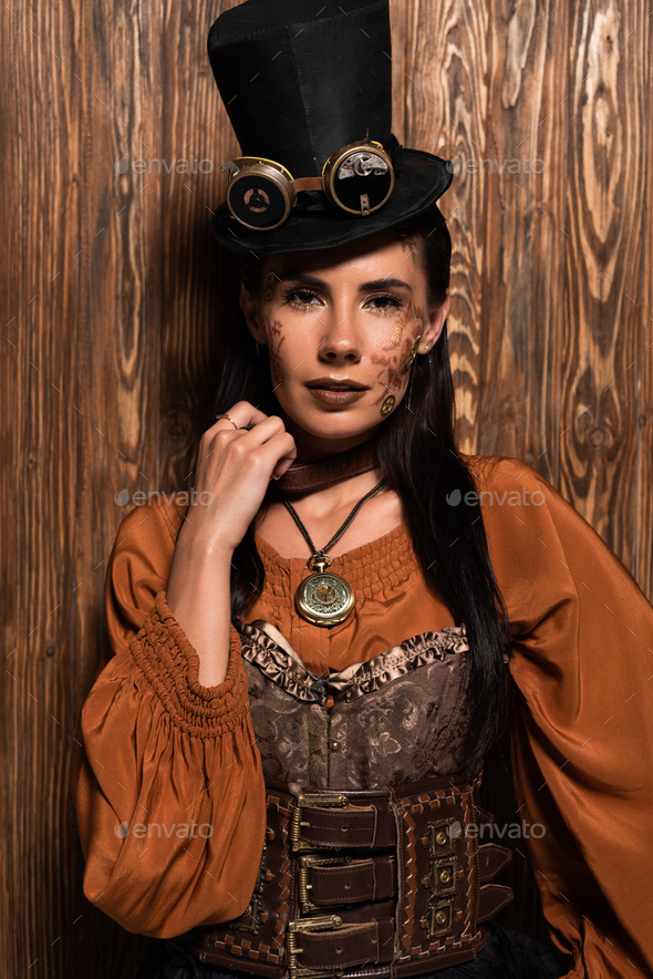 front view of steampunk woman in top hat with goggles looking at camera on wooden