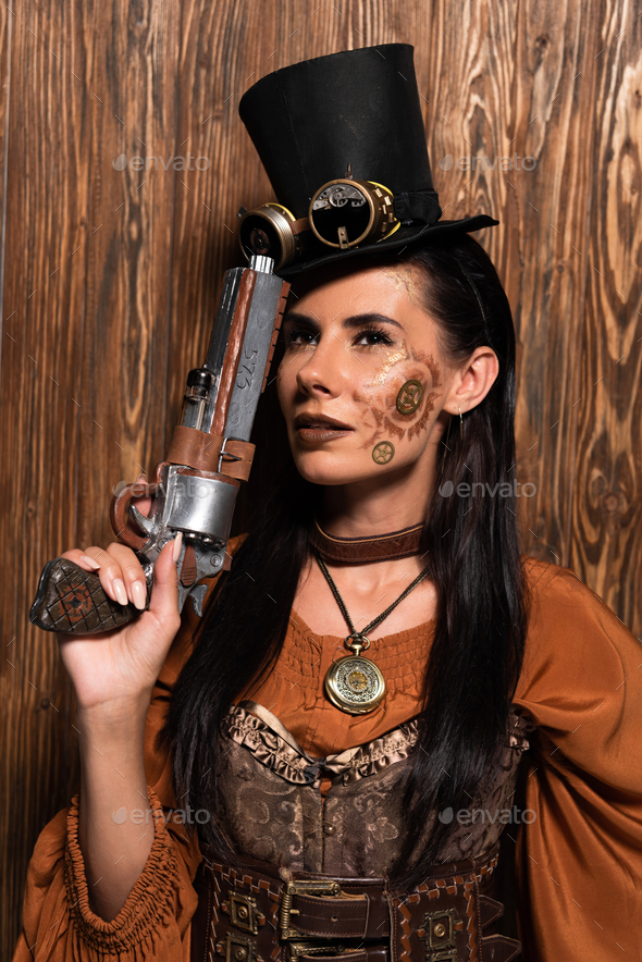 pensive steampunk woman in top hat with goggles holding pistol on wooden