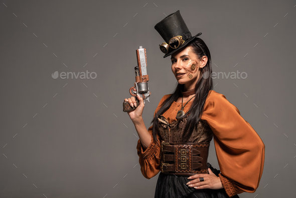smiling steampunk woman in top hat with goggles standing with hand on hip and holding pistol