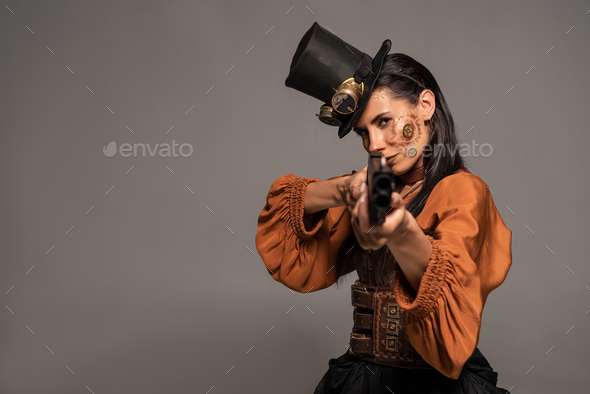 focused steampunk woman in top hat aiming with gun isolated on grey