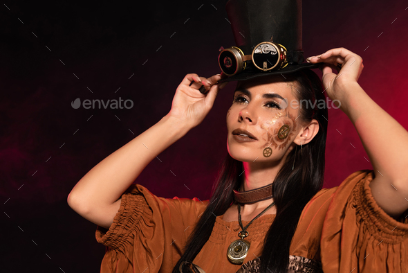 attractive steampunk woman with makeup putting on top hat on black in pink smoke