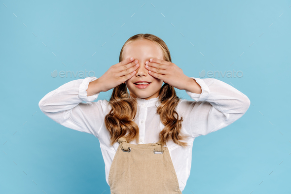 smiling and cute kid obscuring face isolated on blue