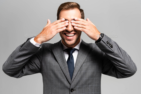 smiling businessman in suit obscuring face isolated on grey