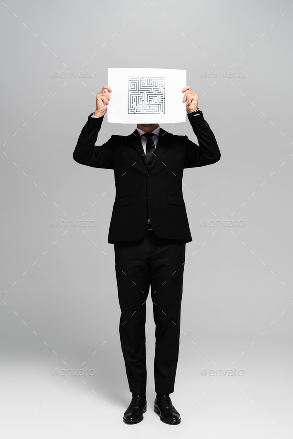 businessman obscuring face with paper with labyrinth on grey background