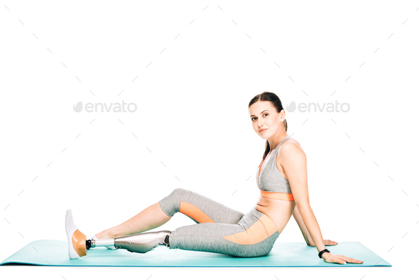 disabled woman in sportswear sitting on fitness mat isolated on white