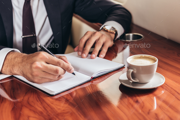 cropped view of businessman writing in notebook in private plane