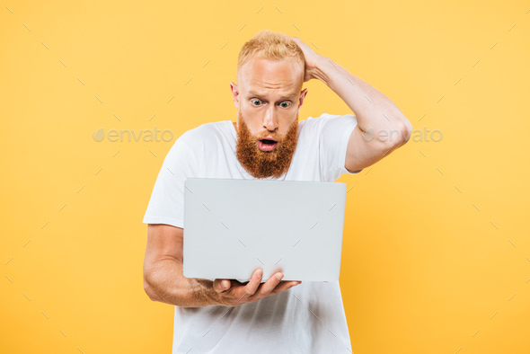 worried bearded man using laptop, isolated on yellow