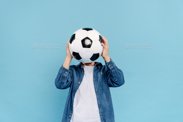 kid obscuring face with football isolated on blue