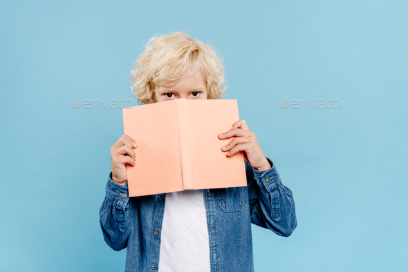 cute kid obscuring face with book isolated on blue