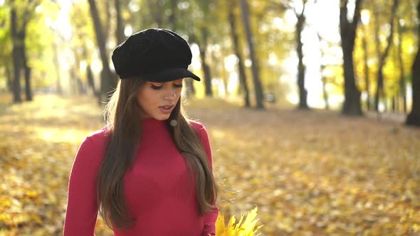 Pretty Longhaired Brunette Poses with Maple Leaves in a Sunny Autumn Park