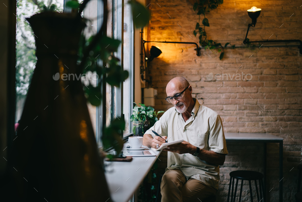Elderly Caucasian author editing notes in cafeteria