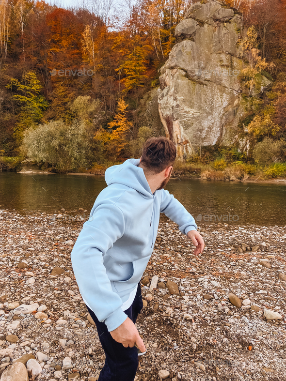 man throwing rocks into river autumn season