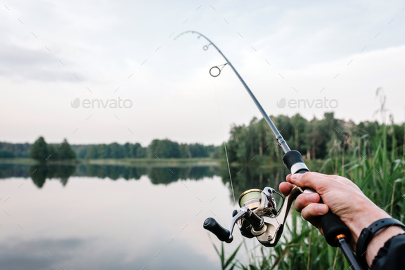Fisherman with rod, spinning reel on the river bank. Fishing for