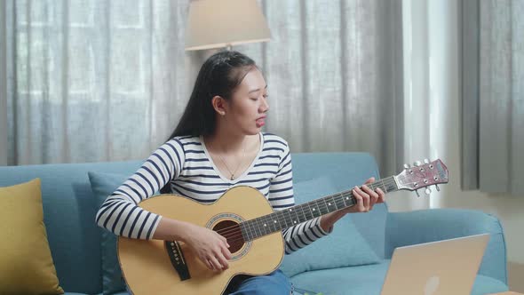 Asian Woman With Laptop Singing And Playing Guitar At Home alt
