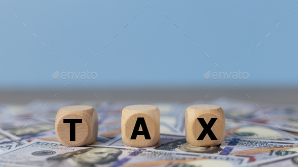 Tax word on wooden cubes on the background of dollar banknotes. Tax payment reminder