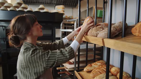 Woman Putting Fresh Bread on Display Rack in Bakery alt