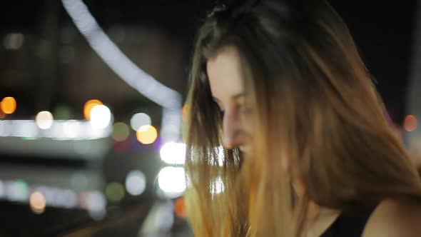 Teenage girl looking at city lights and then smiling at camera at night