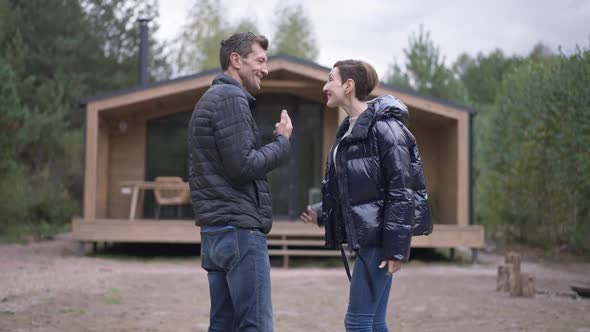 Excited Loving Adult Couple Talking Admiring Wooden Town House Outdoors alt